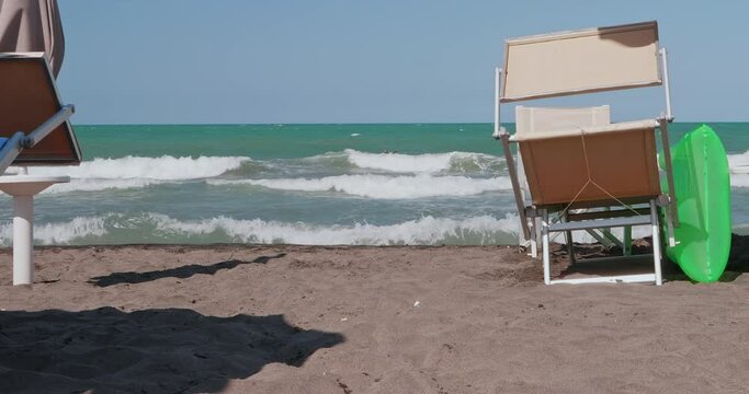 Chair and sunbed on the shoreline of a beach. The sea is rough and there is wind