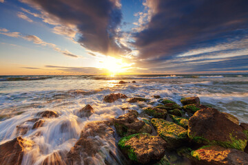 Fototapeta premium Golden splashing waves toward beach shore with rocks and sunrise sea horizon