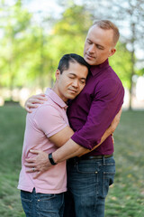Attractive homosexual family, gay couple hugging with closed eyes standing in park on urban street