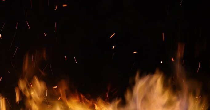 Fire and sparks at night close-up, slow motion. The flames of burning wood log fire on black background