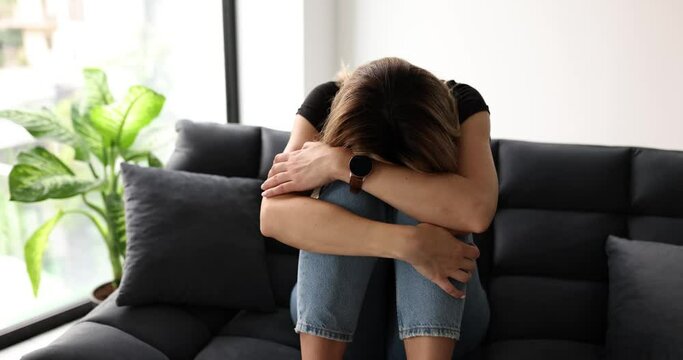 Sad woman sitting on sofa at home and crying 4k movie slow motion. Stress and depression concept