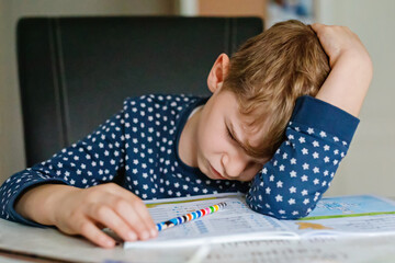 Hard-working sad school kid boy making homework. Upset tired child on home schooling, learning.