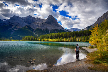 Hiker enjoys the view of Rundle Forebay Reservoir in Canmore, Canada, with Rundle Mountain in the background. - obrazy, fototapety, plakaty