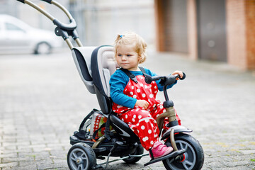 Cute adorable toddler girl sitting on pushing bicycle or tricycle. Little baby child going for a...