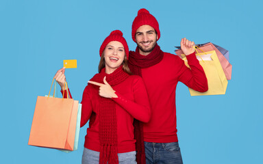 Happy Couple Wearing Winter Hats Posing With Credit Card And Shopping Bags