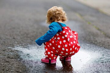 Little toddler girl wearing rain boots and trousers and walking during sleet, rain on cold day....