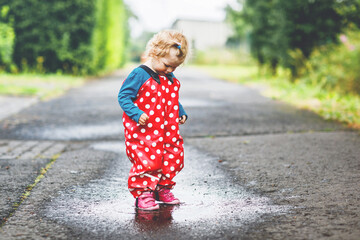 Little toddler girl wearing rain boots and trousers and walking during sleet, rain on cold day....