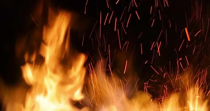 Fire and sparks at night close-up, slow motion. The flames of burning wood log fire on black background