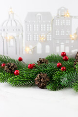 New Year's greeting card with fir branches and red berries on the background of a wooden city