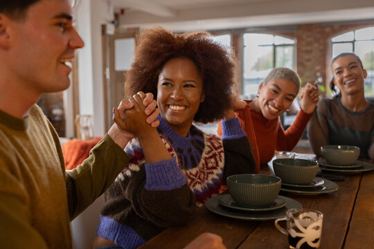 Group of young friends holding hands together during a celebratory meal