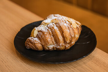 Almond croissant with almond cream filling dusted with icing sugar on a black plate