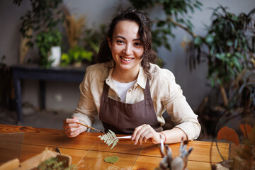 Cheerful asian florist holding dried plant for herbarium in glass frame in floral shop