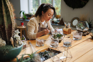 Asian female florist making florarium with succulents near gardening tools in flower shop