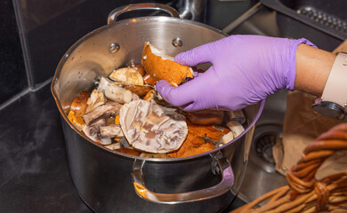 Close-up view of female hands in rubber gloves cleaning mushrooms in kitchen sink.
