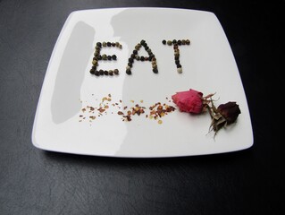 Plate with word `eat` made of black pepper, red chili pepper flakes and pink dried rose buds