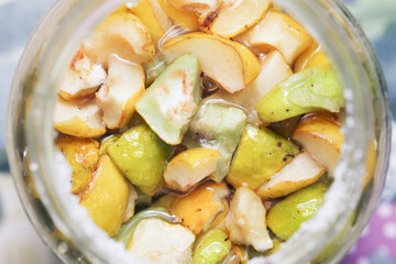 Quince in glass jar. Sugar covered fruits releases juice. Marinating fruits background. Quince tincture production. Homemade fruit alcohol. Top view round open jar.