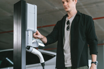 Young man travel with EV electric car to shopping center parking lot charging in downtown city...