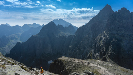 Tatry Wysokie, Rysy, zejście ze szczytu po stronie Słowackiej, w piękny letni dzień. Turystka z pomarańczowym plecakiem i kaskiem - obrazy, fototapety, plakaty