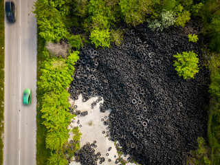 Aerial view of the stark contrast between a massive landfill of used car tires and the surrounding...