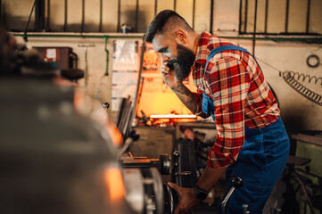 A metal turner using calipers to measure width of a cylinder in a factory.