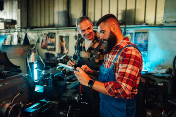 Two metallurgists talking about a metal cylinder next to a lathe machine.