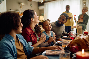 Happy multiracial extended family has fun and laughs while gathering for Thanksgiving in dining room.