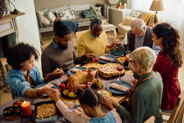 Multiracial extended family holding hands while sitting at dining table and praying before...