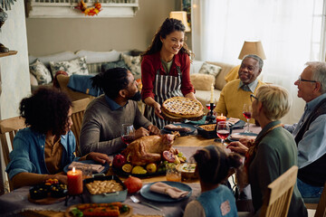 Happy woman serving Thanksgiving pie to her extended family during meal at dining table.