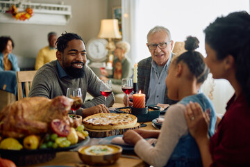 Fototapeta na wymiar Happy black man talks to his family during Thanksgiving dinner in dining room.