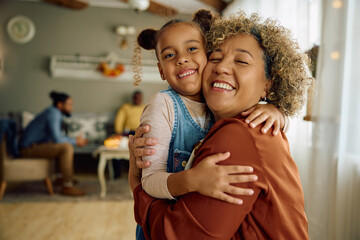 Happy black little girl and her grandmother embracing at home and looking at camera.