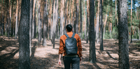 Fototapeta premium Portrait from the back of a young man with a backpack on a walk in a pine forest on a sunny day.