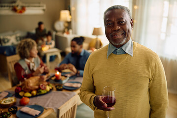 Senior black man enjoying in Thanksgiving family gathering at home and looking at camera.