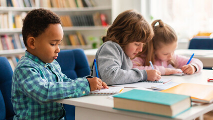 Fototapeta na wymiar Diverse primary school children writing in copybooks during a test