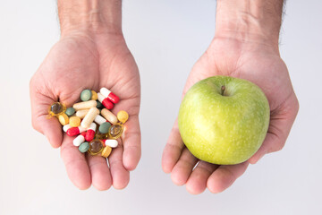 man's hand with one with a green apple and hand with pills 
