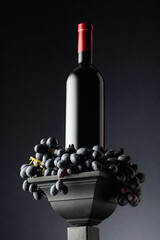 Blue grapes and a bottle of red wine on a black background.