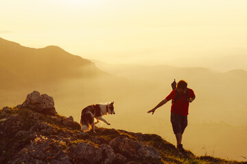 young man with his border collie dog hiking in the mountains at sunset. sport and adventure.