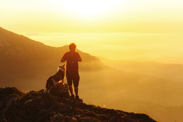 young man with his border collie breed dog, in the mountains contemplating the sunset. Person...