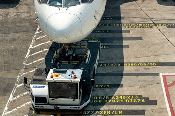 High angle view of aircraft parked at jet bridge on yellow airport gate markings on the tarmac in front of gate with pushback tractor or airport tug in front