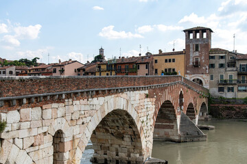 Fototapeta na wymiar Side view of Ponte Pietra bridge over the Adige River in Verona, Italy with ancient houses along embankment the river