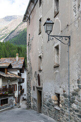 View down a narrow street lined with medieval buildings in the city of Cogne, Italy with mountains in the background