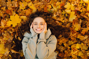 Smiling young woman lies on the autumn foliage in the forest with the yellow leaves