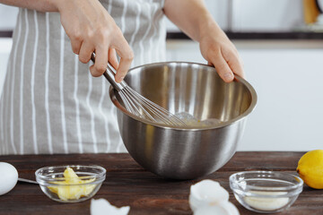 A cook in an apron kneads the dough in a bowl using a whisk for baking bread, dessert, pie, buns. Homemade or handmade bread, dessert. Kitchen background.