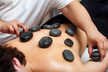 Hot stone massage therapy. Doctor therapist make hot stones massage on man back, massaging body. Handsome male visit masseur in medical clinic room. Alternative medicine concept. Copy ad text space
