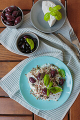 Feta cheese sliced on blue plate with sesame, flax seeds, served with black olives and basil leaves. Delicious and healthy breakfast on terrace