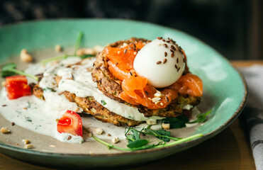 Vegetarian zucchini pancakes with poached egg, salmon and tomato, close up, healthy breakfast.