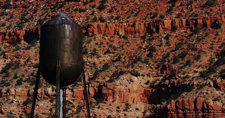 Old water tower, composed before a cliffside of red rocks and sandstone, wavers in the desert heat.