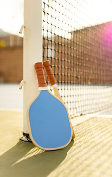 Photograph of two pickleball rackets resting on the net post of a sports court at sunset. Pickle ball concept. Sports similar to tennis.