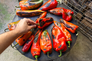 Red peppers arranged on the stoves burner, fired by wood. A hand turns them. Its an autumn day, and the process takes place outdoors in the yard. Concept of preparing preserves and ajvar