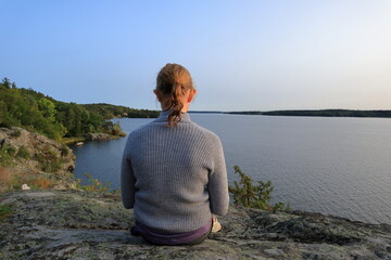 Girl at a cliff looking into the sea and horizon. Mälaren lake, Sweden.