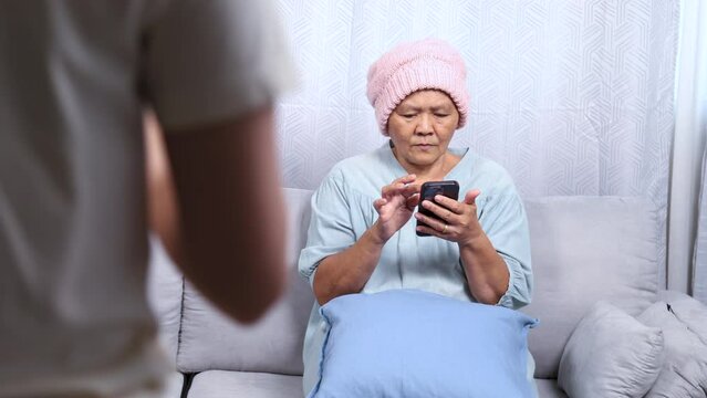 Young Asian daughter supports mother breast cancer patient wearing headscarf during chemotherapy treatment period hair fall, female take care mom encourage to drink dairy milk to elderly tenderness
